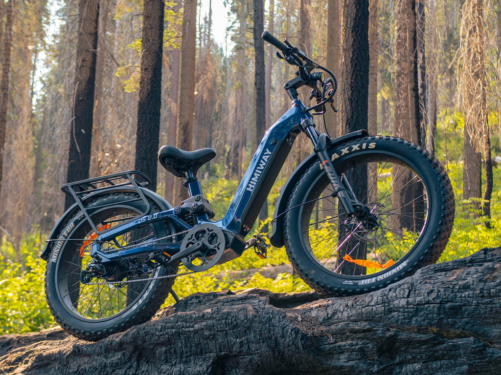A Midnight Blue Himiway D5 2.0 step-thru fat tire electric bike parked on a large fallen log in a dense forest.